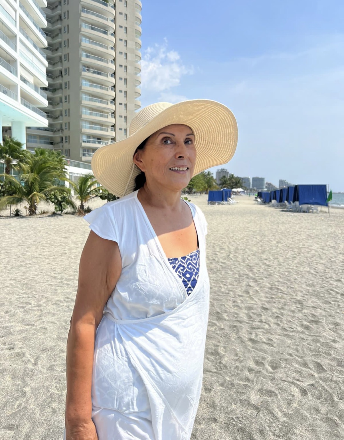 Una mujer mayor camina por la playa con sombrero